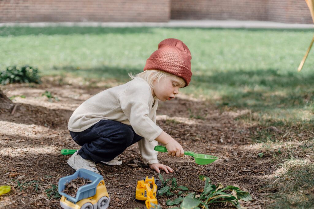 Mains d'enfants manipulant des bâtons et des feuilles dans la cour d'une garderie, utilisant ces éléments pour un jeu imaginaire stimulant le vocabulaire et la narration.